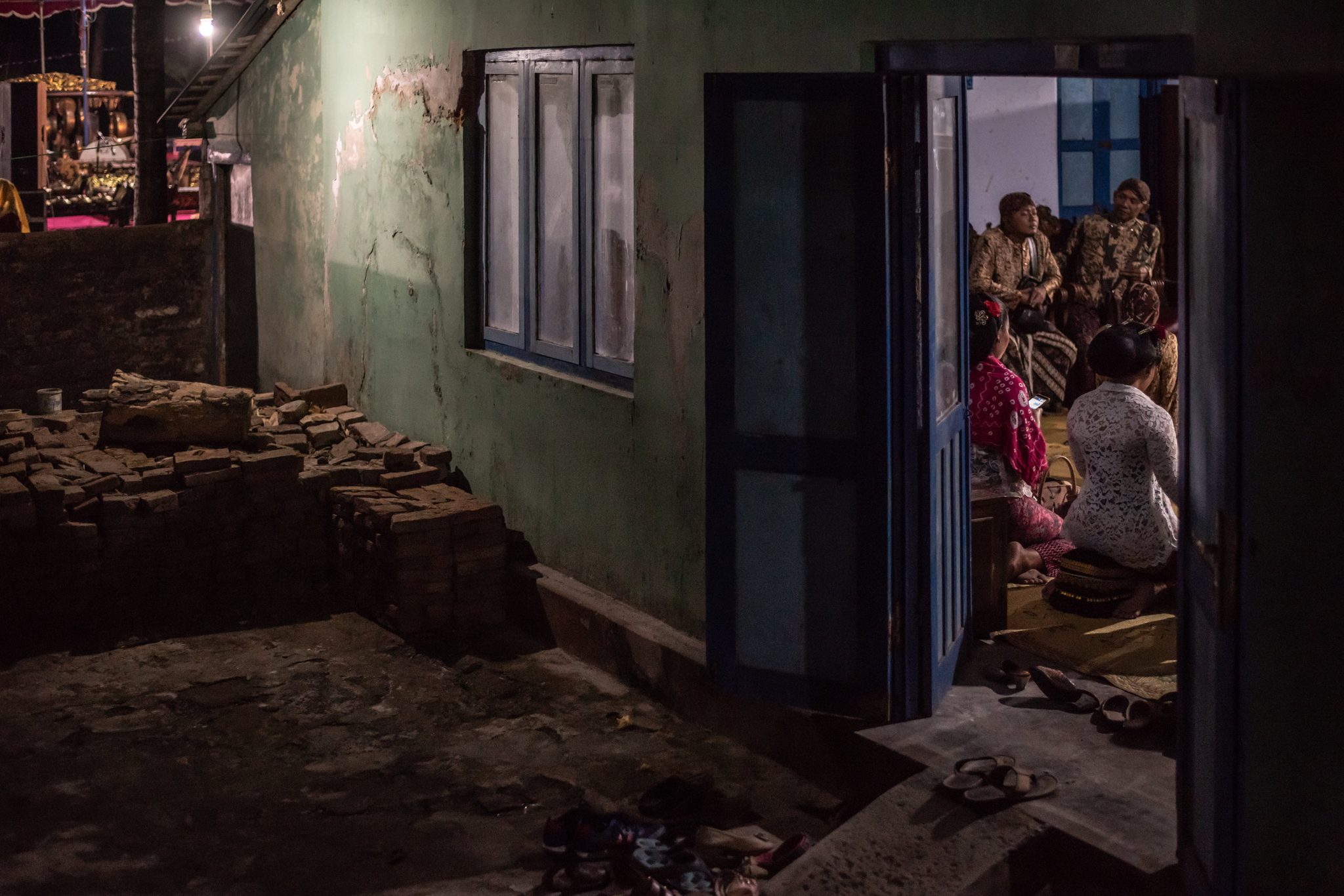 Through an open door, the performers wait in the lamplight. Outside, the night stays dark.