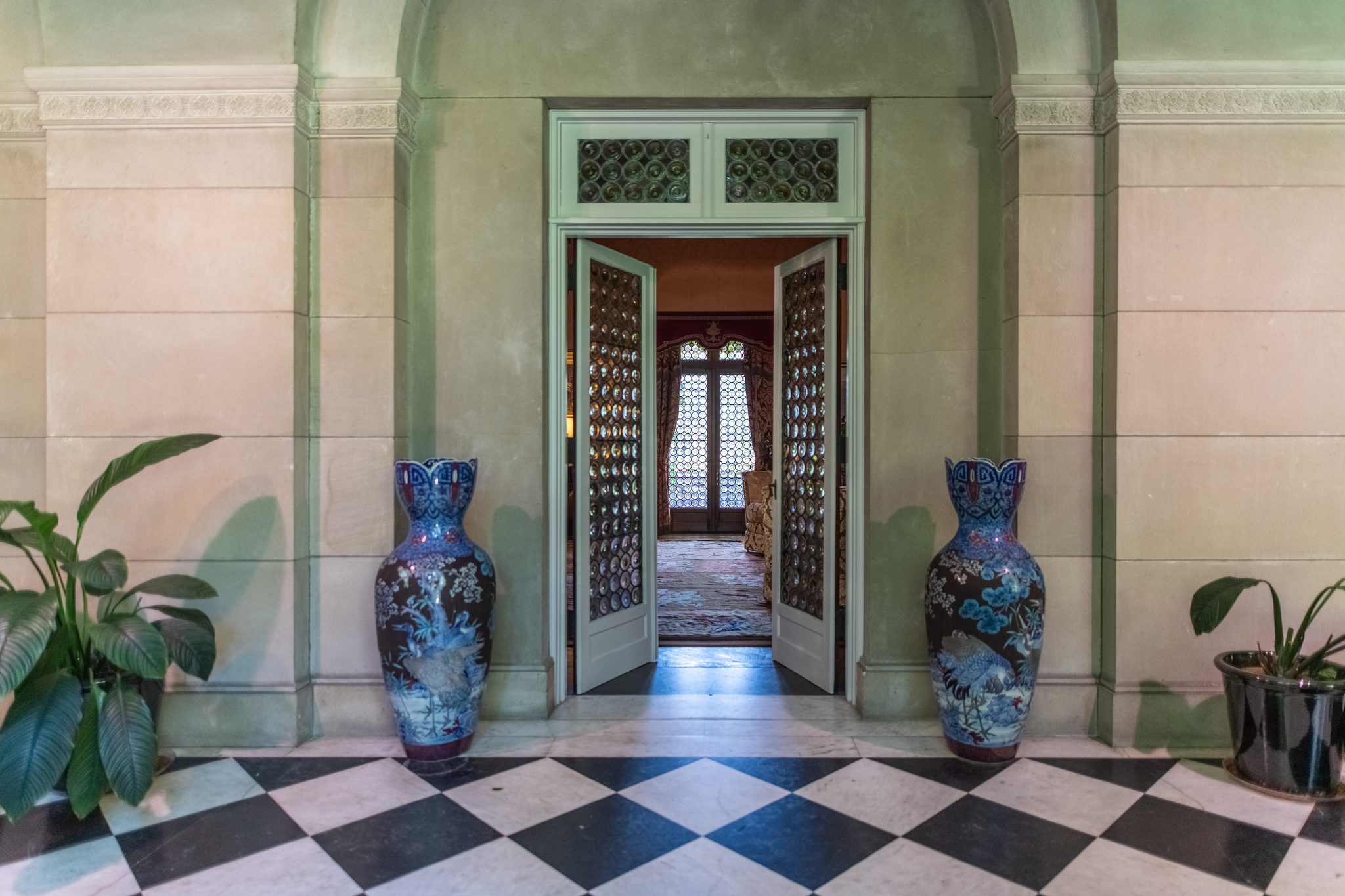 Twin tall blue vases flank open grille doors in a stone vestibule, the checkerboard marble floor cool in mid-June.