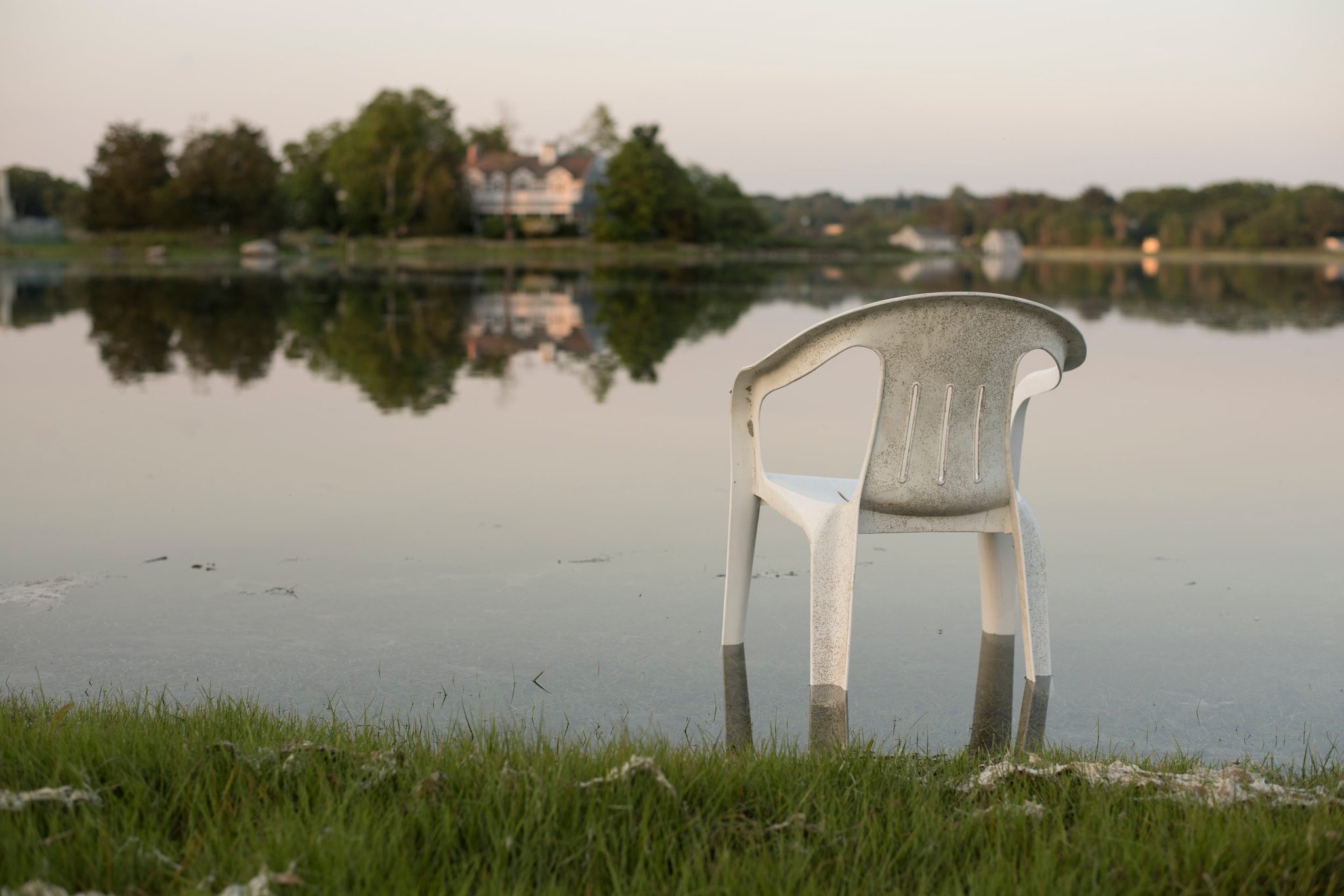 A plastic chair stands ankle deep in the flooded lawn, the water still as glass.