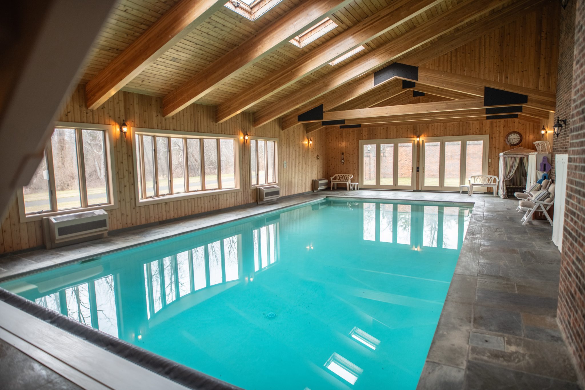 A skylit timber roof and flagstone deck keep a March swim bright in this indoor pool house.