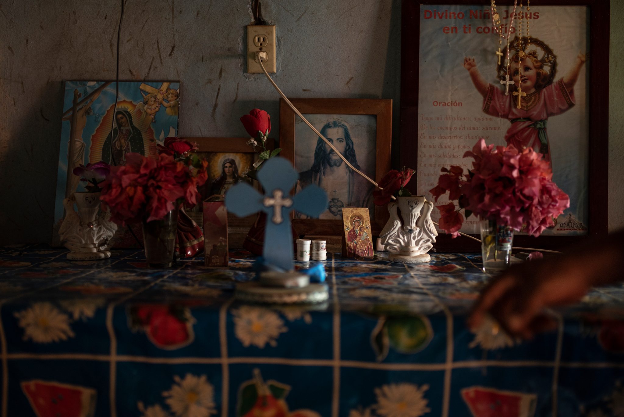 A home altar holds the Virgin of Guadalupe, Christ and a blue cross among the flowers.