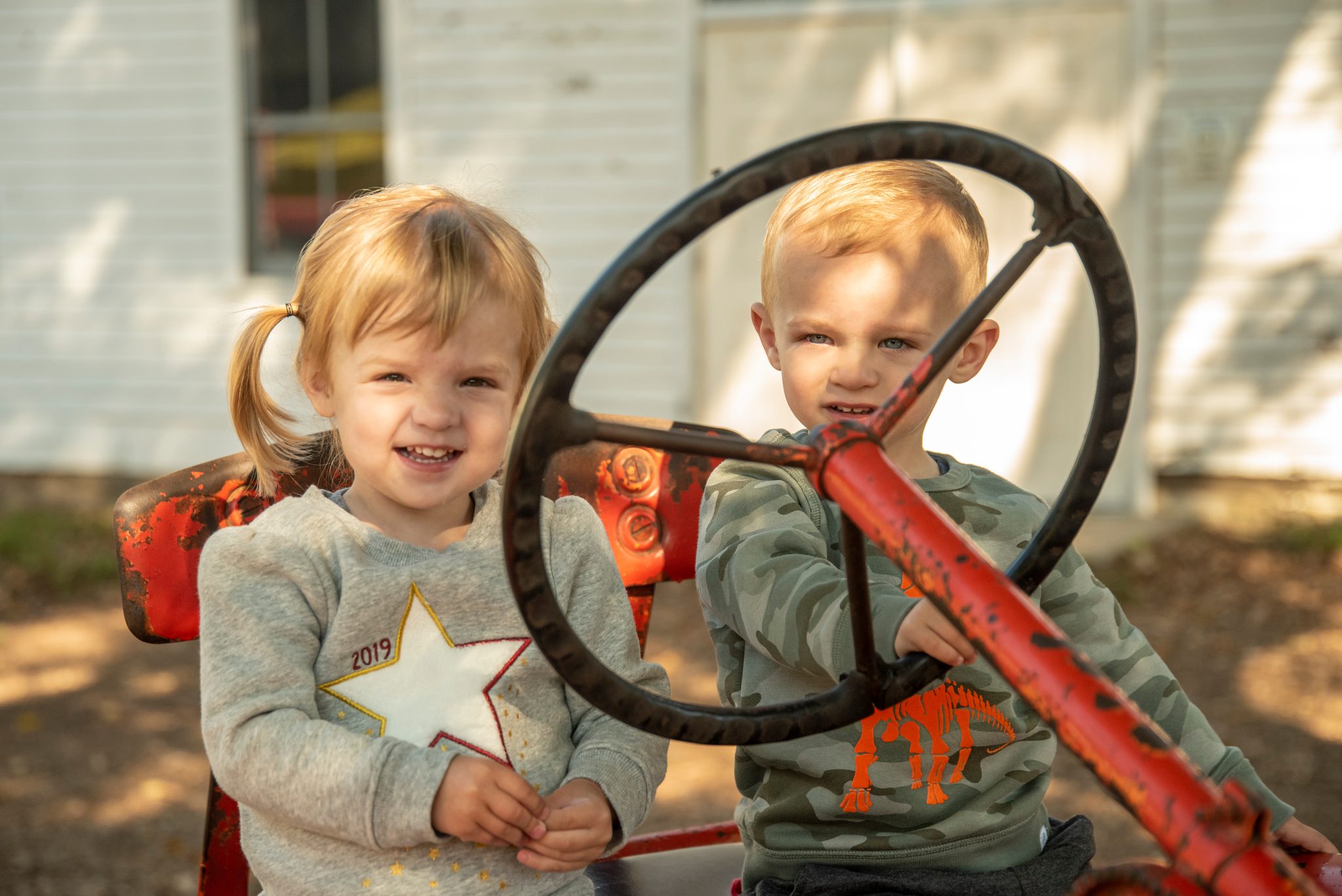 Two toddlers take the wheel of an old red tractor, neither one ready to give it up.