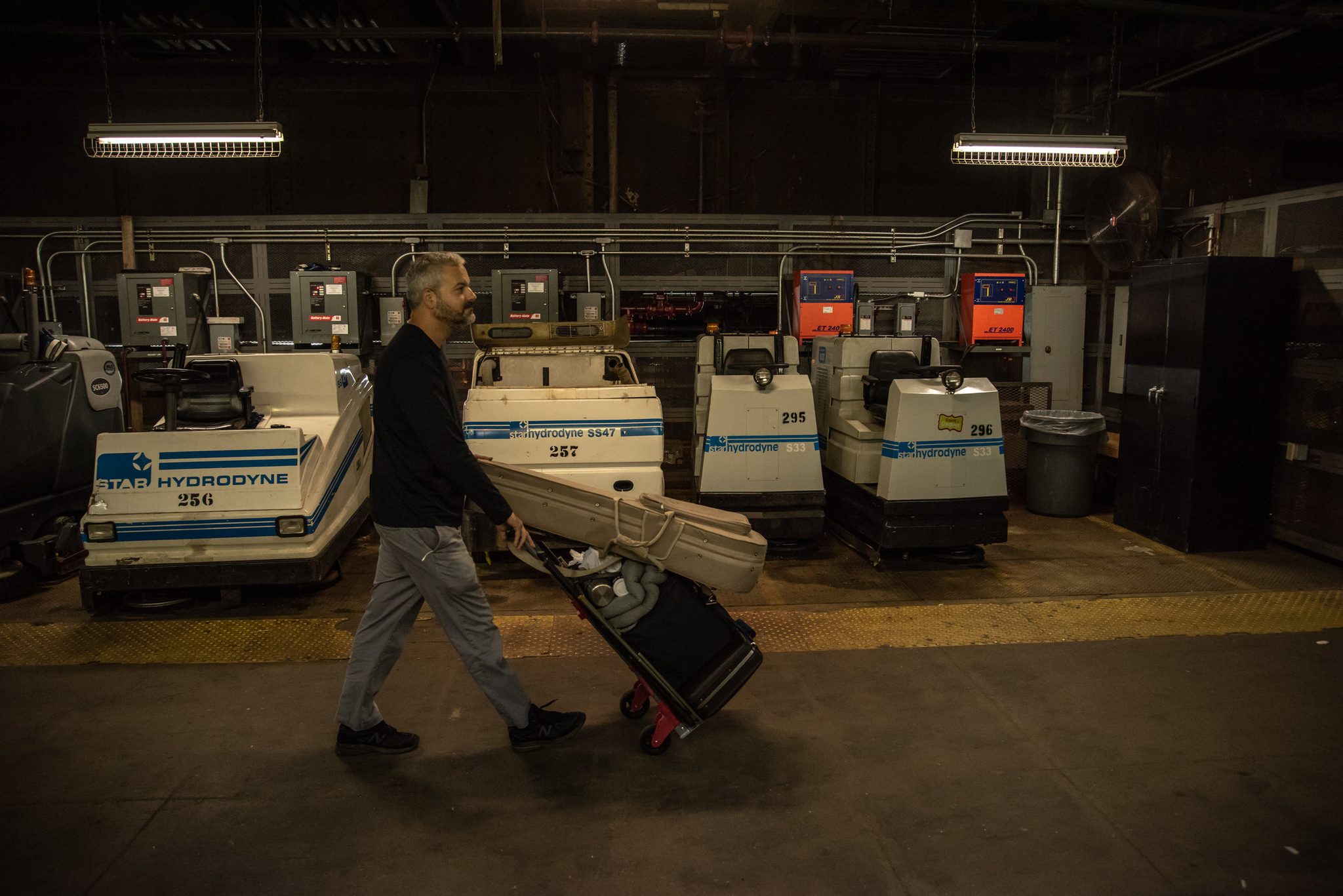 Glenn wheels his gear past a row of parked floor scrubbers deep in the station.