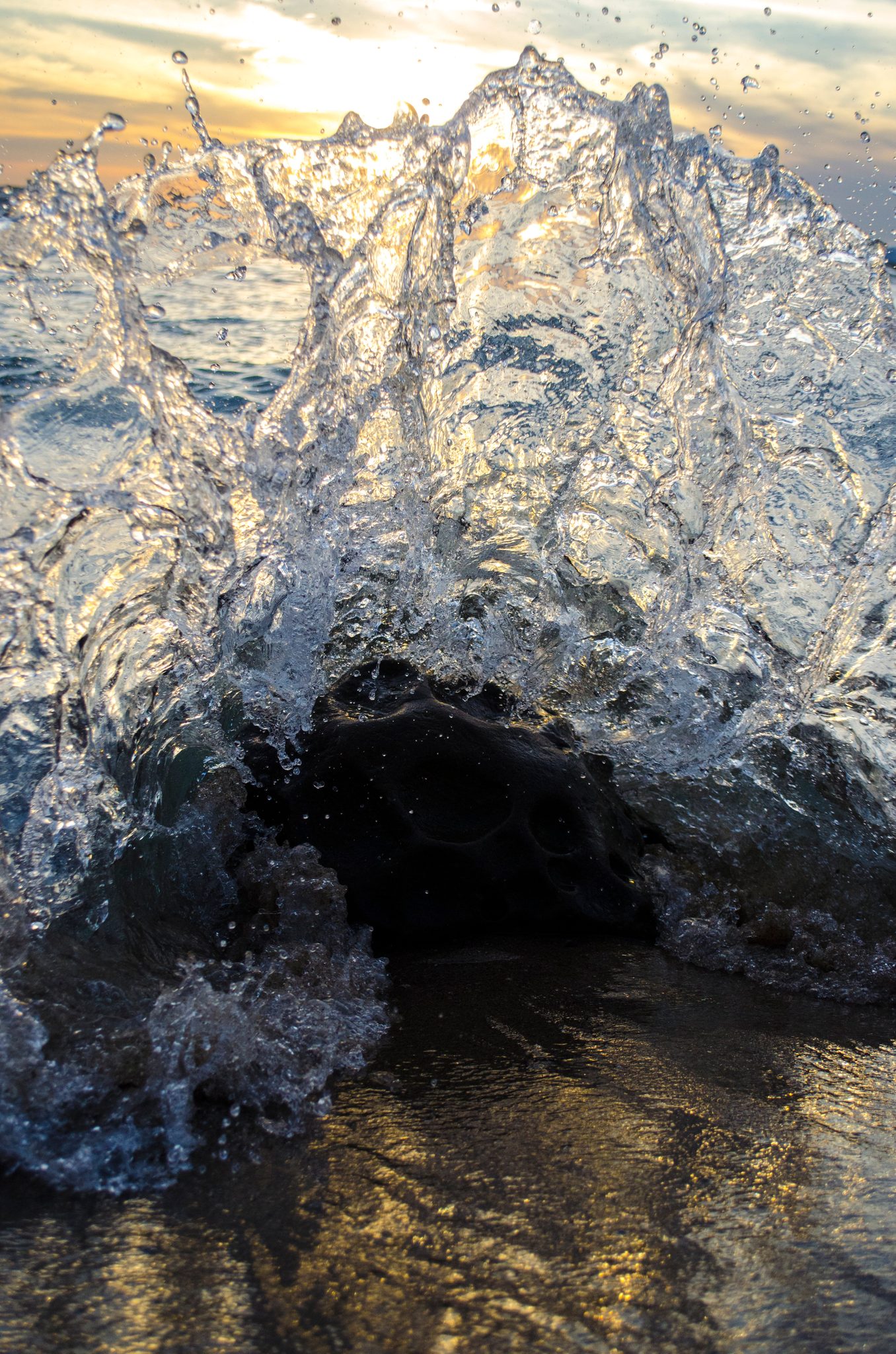 A wave bursts upward, backlit by the setting sun.