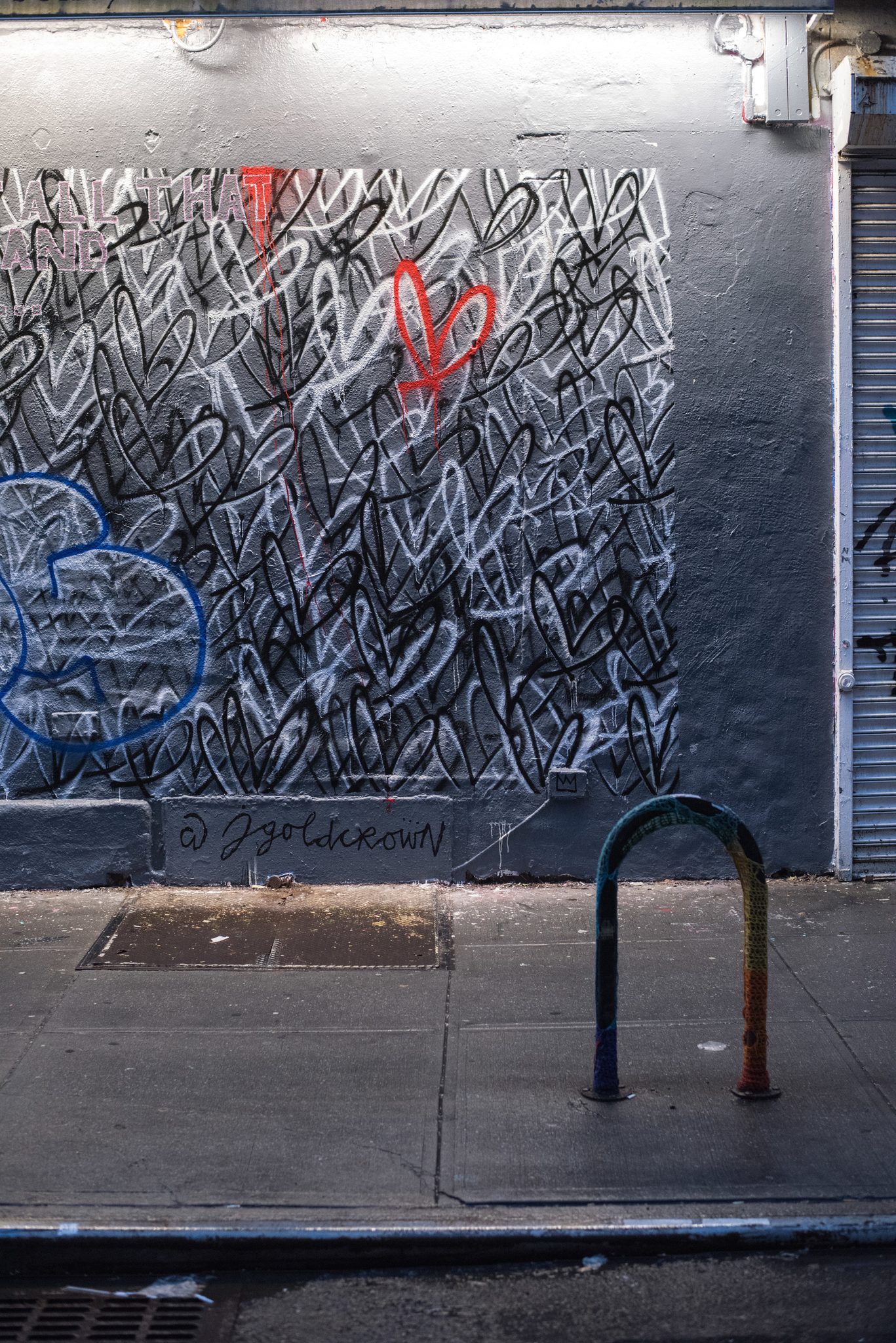 A wall of scrawled hearts, one of them red, above an empty sidewalk.