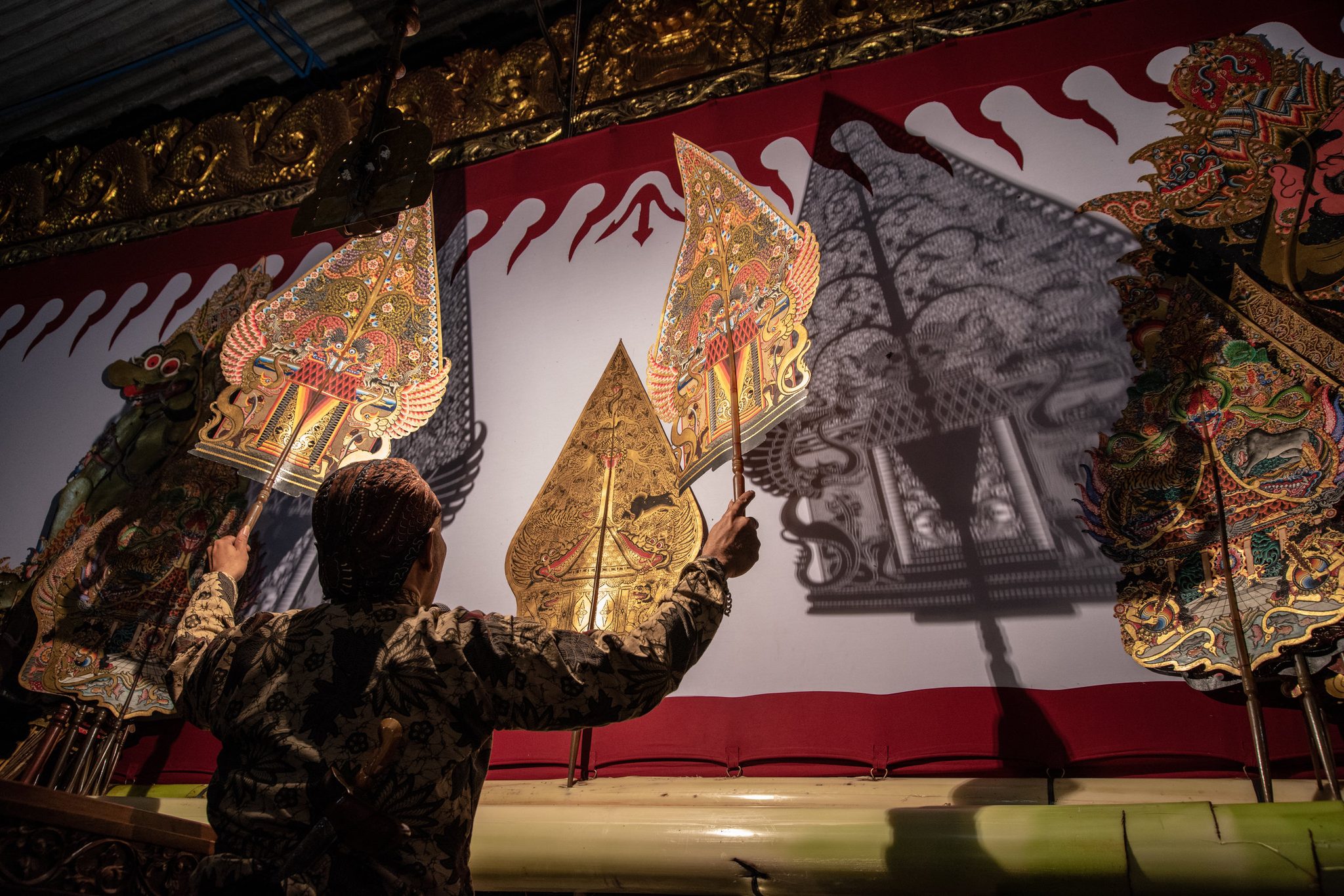 Ki Seno lifts two puppets to the screen, their shadows joining the painted ones behind.